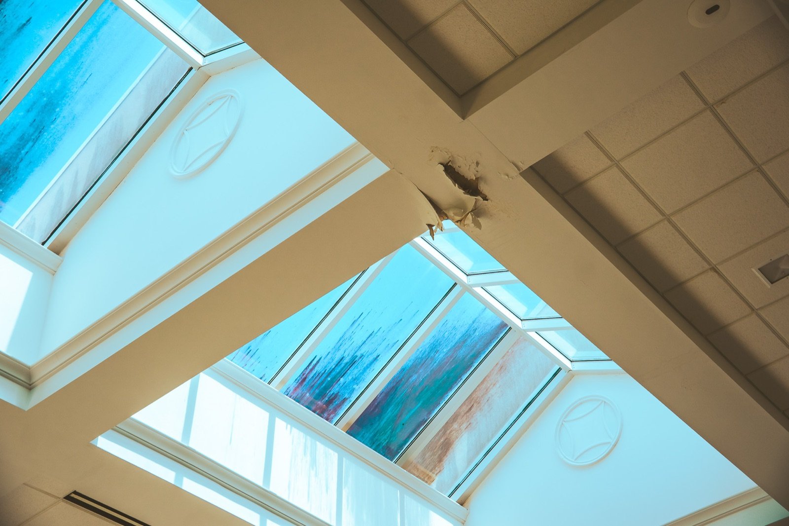 Atrium skylights with heavy water staining on the glass and a hole where the sheetrock below has failed